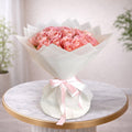 Bouquet of pink roses wrapped in white paper with a pink ribbon on a marble table.