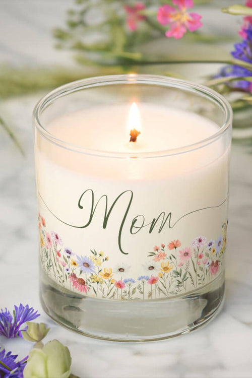 Candle with 'Mom' and floral design on a marble surface with flowers in the background