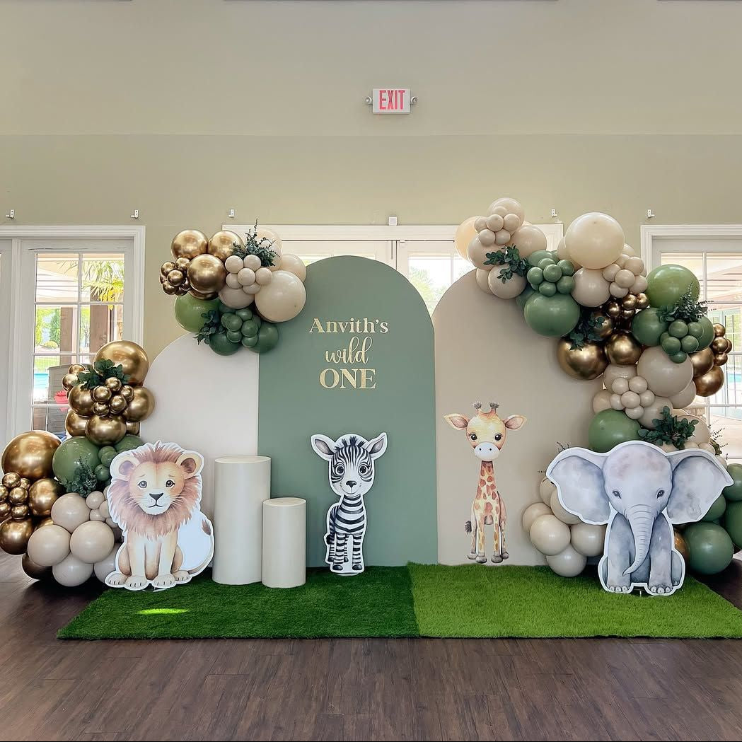 Wild One jungle safari 1st birthday stage decoration in Dubai featuring sage green arches, chrome gold balloon garland, and cute safari animal cutouts.