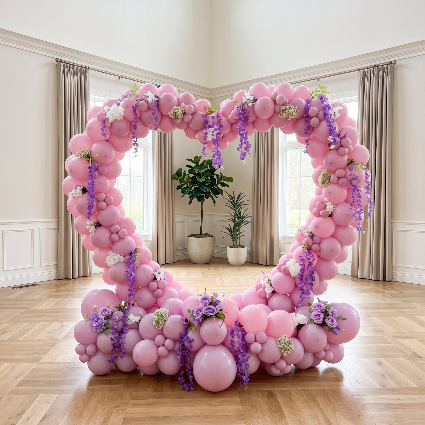 A large heart-shaped balloon arch decoration made of pink balloons with purple floral accents, displayed in a bright, high-ceilinged room with wood floors and windows.