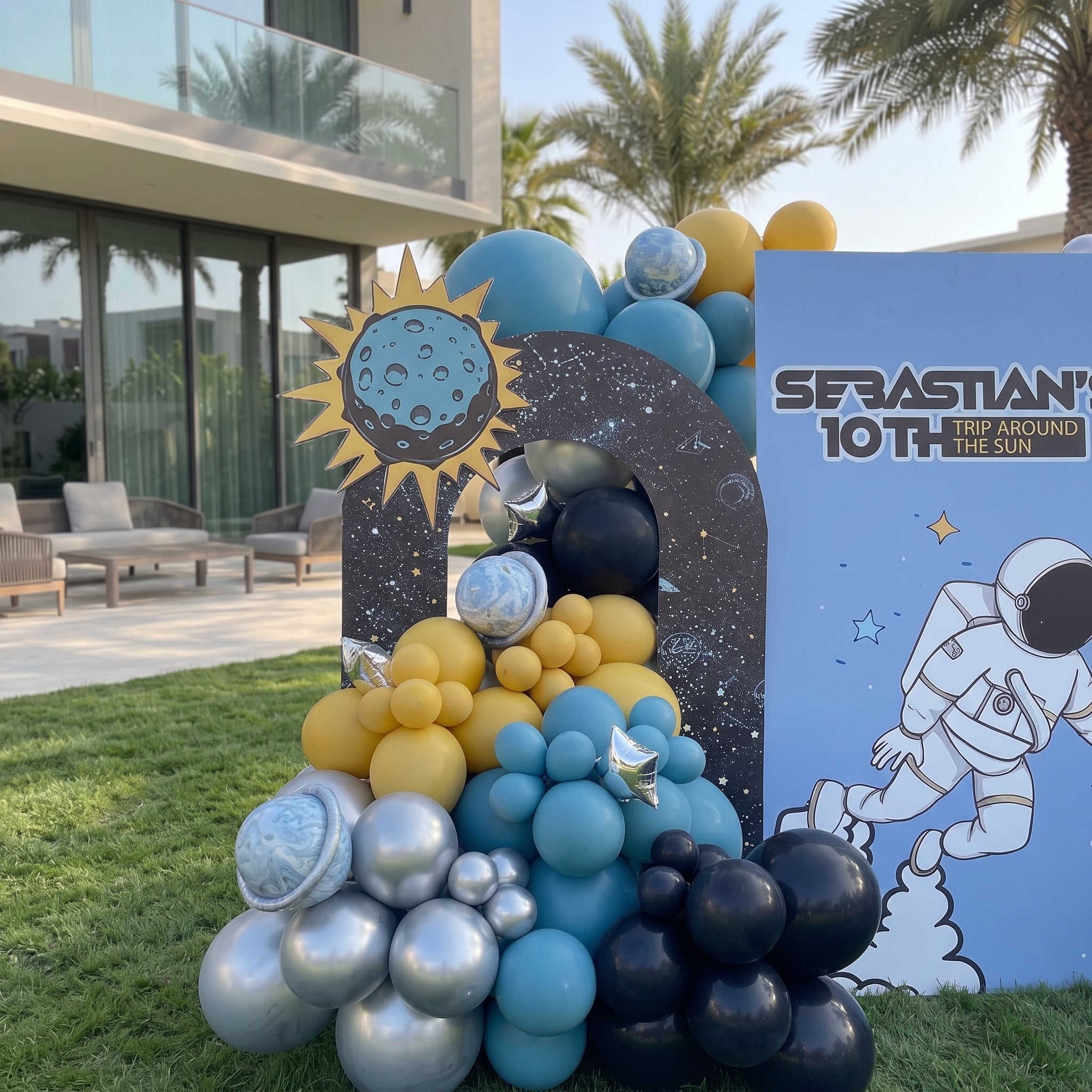 Outer space themed Trip Around the Sun birthday backdrop in Dubai with astronaut board, rocket arch, and blue, yellow, and chrome balloon garland.