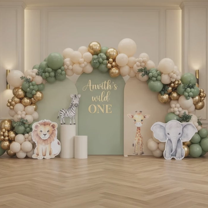 Wild One jungle safari 1st birthday stage decoration in Dubai featuring sage green arches, chrome gold balloon garland, and cute safari animal cutouts.