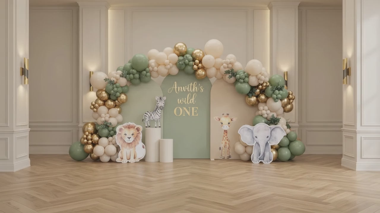 Wild One jungle safari 1st birthday stage decoration in Dubai featuring sage green arches, chrome gold balloon garland, and cute safari animal cutouts.